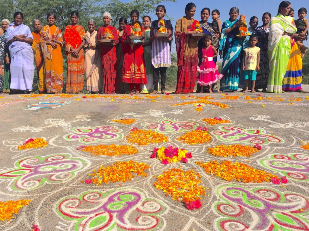 Cholk and flower art on sidewalk in India with brightly dressed women and children.