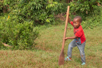 Young boy with garden tool outside in Uganda.