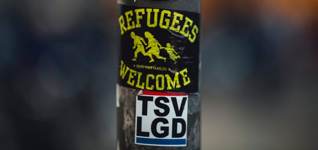 Refugees welcome sticker on a water bottle with other stickers and blurred background.