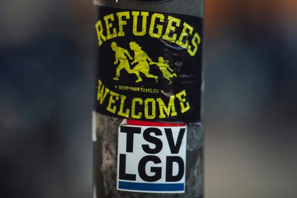 Refugees welcome sticker on a water bottle with other stickers and blurred background.